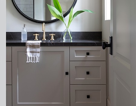 Media room bathroom with custom cabinetry, black marble top, brass fixtures and round mirror in Houston, TX